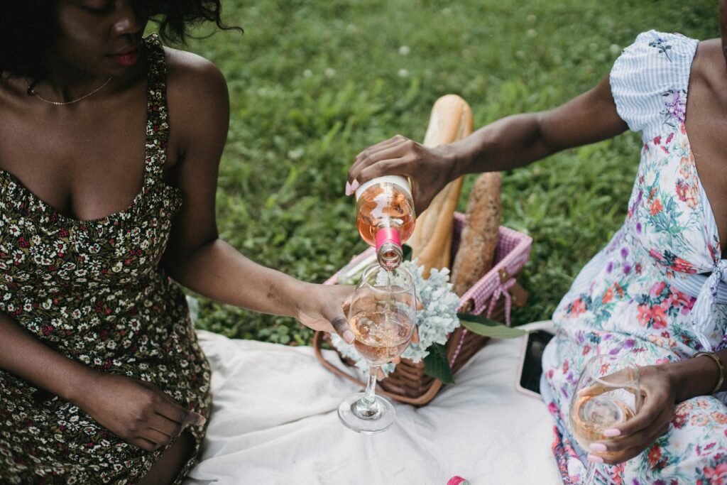 Two women enjoying a picnic with wine in a sunny park setting, capturing summer leisure.